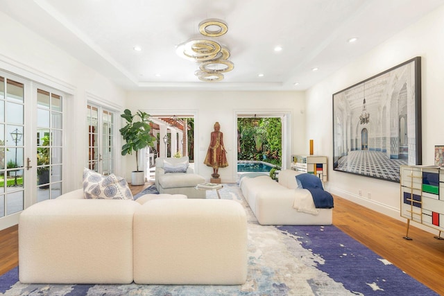 living room with plenty of natural light, a raised ceiling, wood-type flooring, and french doors