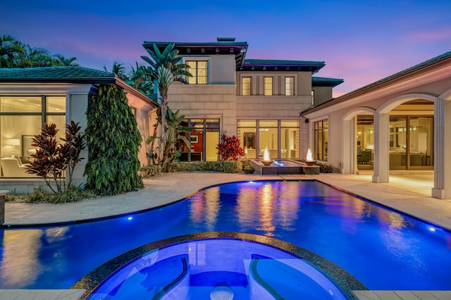 pool at dusk with an in ground hot tub and a patio area