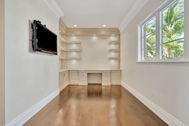 unfurnished office featuring crown molding, hardwood / wood-style floors, and built in desk