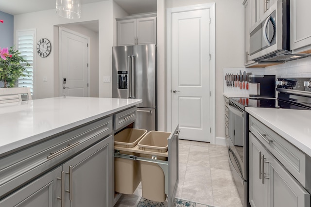 kitchen featuring pendant lighting, light tile patterned floors, gray cabinetry, appliances with stainless steel finishes, and decorative backsplash