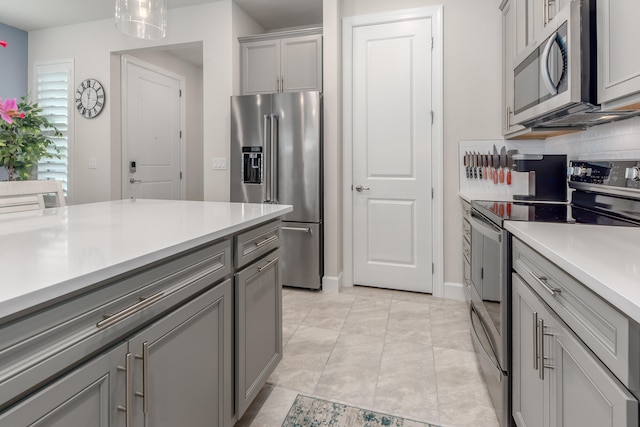 kitchen featuring gray cabinets, backsplash, appliances with stainless steel finishes, light tile patterned floors, and decorative light fixtures