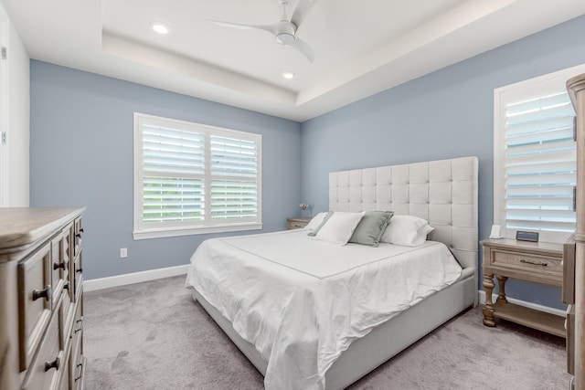 carpeted bedroom featuring a tray ceiling, multiple windows, and ceiling fan