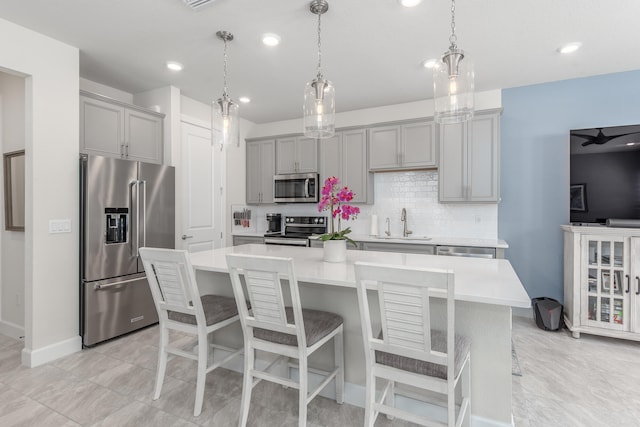 kitchen featuring gray cabinets, stainless steel appliances, a large island with sink, and a kitchen breakfast bar