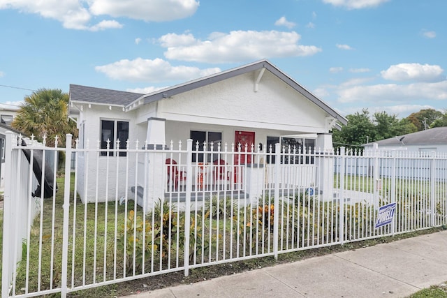 bungalow-style home featuring a shingled roof, a fenced front yard, and stucco siding