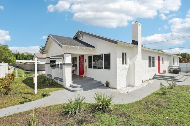 bungalow with stucco siding, a chimney, a front yard, and fence