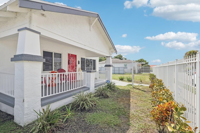 view of property exterior with stucco siding, covered porch, and fence