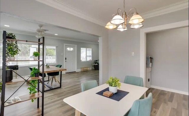 dining room with baseboards, wood finished floors, ornamental molding, and ceiling fan with notable chandelier