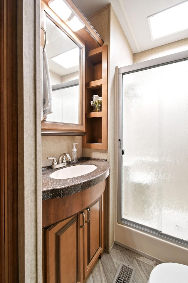 bathroom featuring walk in shower, toilet, and vanity