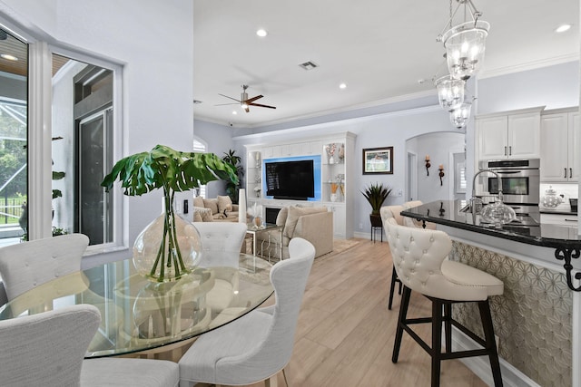 dining area featuring crown molding, light hardwood / wood-style flooring, and ceiling fan with notable chandelier