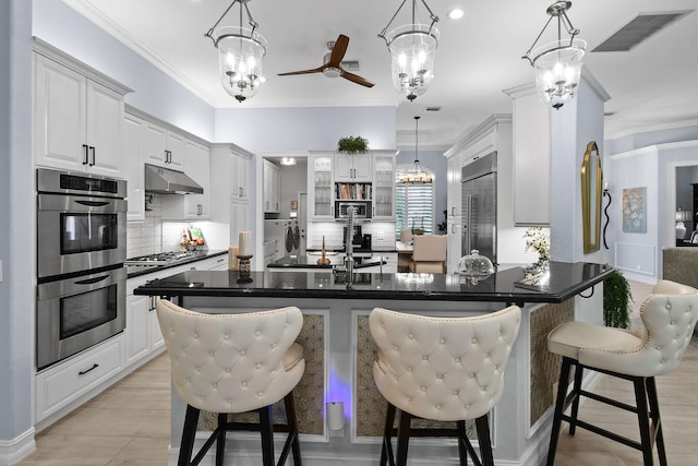 kitchen featuring ceiling fan with notable chandelier, tasteful backsplash, a breakfast bar, stainless steel appliances, and ornamental molding