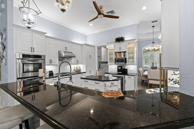 kitchen with ceiling fan with notable chandelier, hanging light fixtures, stainless steel appliances, decorative backsplash, and white cabinetry