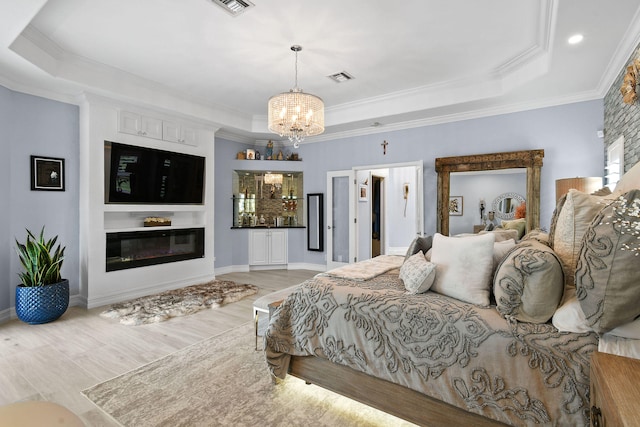 bedroom featuring a tray ceiling, crown molding, light hardwood / wood-style flooring, and a notable chandelier