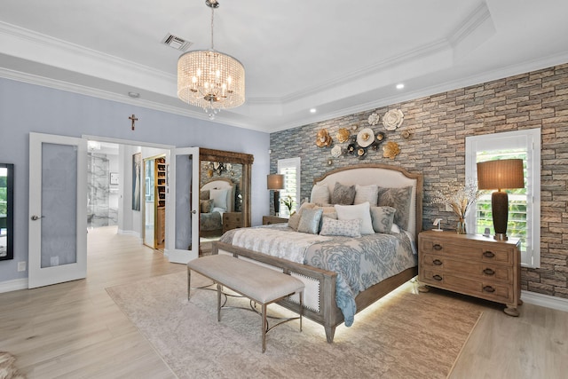 bedroom featuring a tray ceiling, ornamental molding, light hardwood / wood-style flooring, and a walk in closet