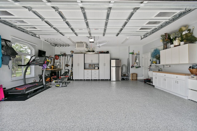 garage with an AC wall unit, stainless steel refrigerator, and a garage door opener