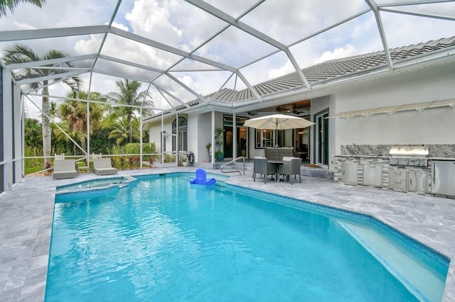 view of swimming pool with grilling area, a patio area, glass enclosure, ceiling fan, and an outdoor kitchen