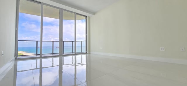 unfurnished room featuring tile patterned flooring, a water view, a wall of windows, and a beach view