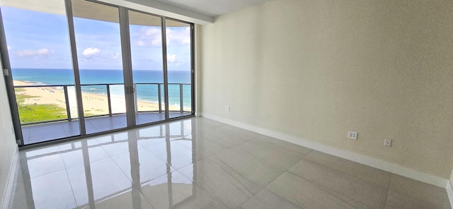 tiled spare room with a beach view, a water view, and a wall of windows