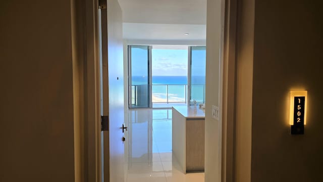 corridor with expansive windows, plenty of natural light, a water view, and light tile patterned floors