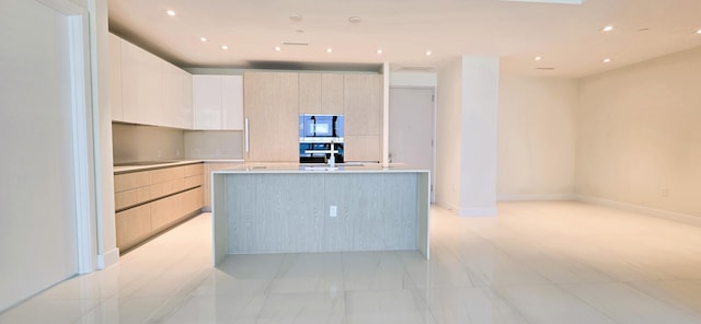 kitchen with white cabinetry, light brown cabinets, sink, oven, and a kitchen island with sink