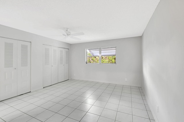 unfurnished bedroom featuring ceiling fan, light tile patterned flooring, a textured ceiling, and multiple closets