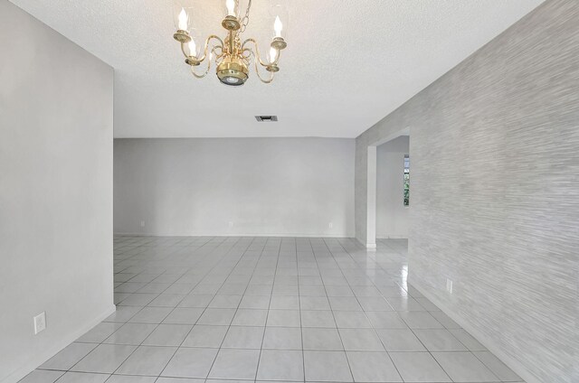 tiled spare room with a chandelier and a textured ceiling