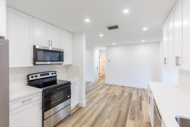 kitchen with appliances with stainless steel finishes, white cabinetry, and light hardwood / wood-style flooring