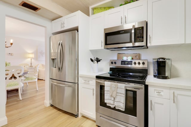 kitchen with light wood-type flooring, appliances with stainless steel finishes, an inviting chandelier, and white cabinetry