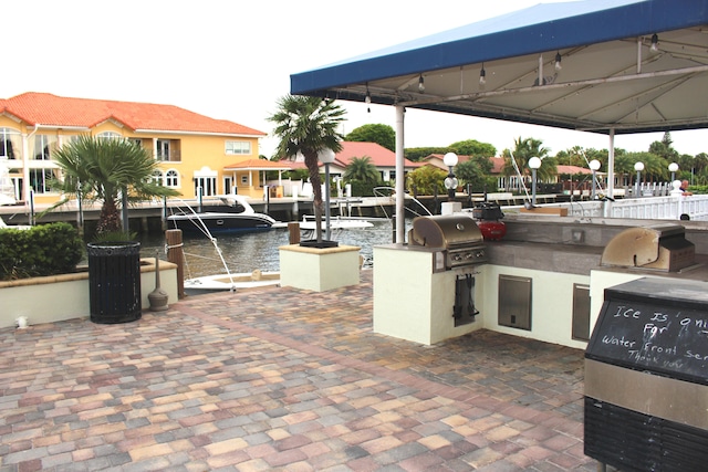 view of patio featuring exterior kitchen, a water view, area for grilling, and a gazebo