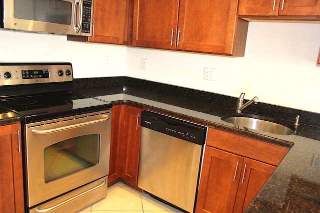 kitchen featuring dark stone countertops, light tile patterned flooring, stainless steel appliances, and sink