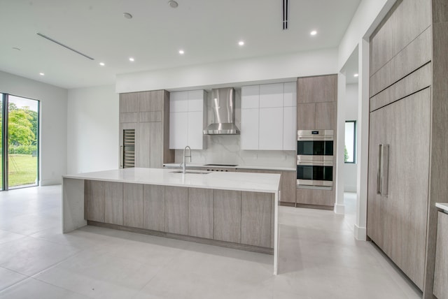 kitchen featuring stainless steel double oven, a spacious island, tasteful backsplash, sink, and wall chimney range hood