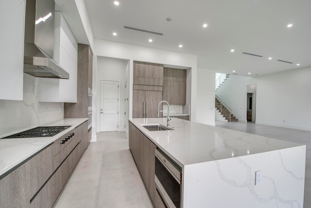 kitchen with light stone counters, sink, wall chimney range hood, a large island, and stainless steel microwave