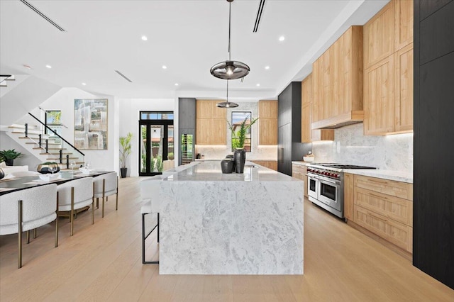 kitchen with light wood-type flooring, pendant lighting, double oven range, and light stone countertops