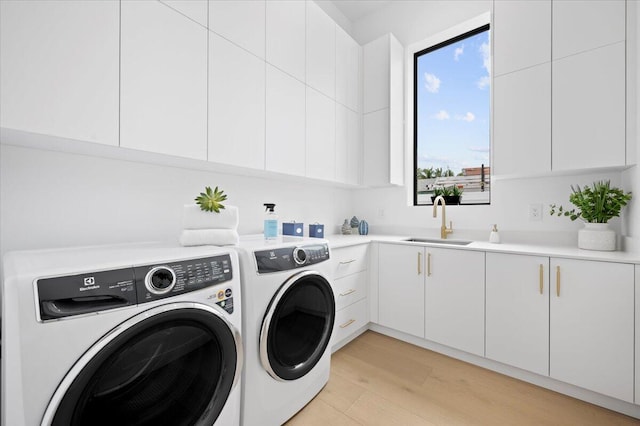 laundry room with light hardwood / wood-style flooring, cabinets, sink, and washing machine and dryer