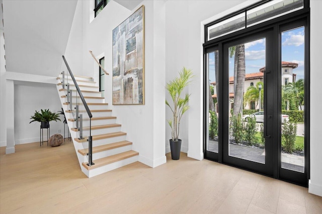 foyer entrance featuring plenty of natural light, a towering ceiling, light wood-type flooring, and french doors