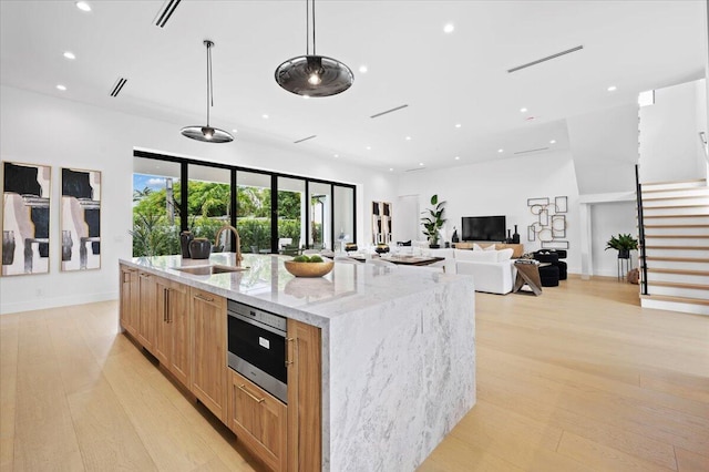 kitchen featuring a large island with sink, pendant lighting, sink, light stone countertops, and light hardwood / wood-style floors