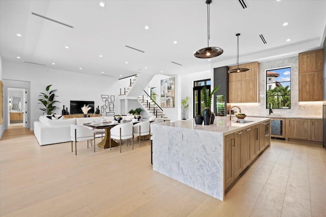 kitchen featuring light wood-type flooring, decorative light fixtures, light stone counters, sink, and an island with sink