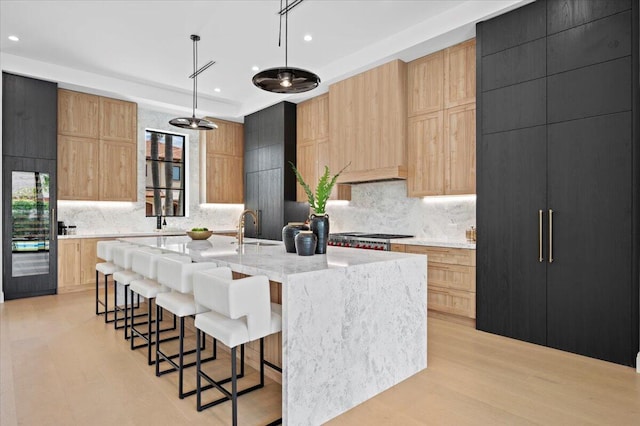 kitchen with light wood-type flooring, decorative light fixtures, light stone counters, sink, and a center island with sink