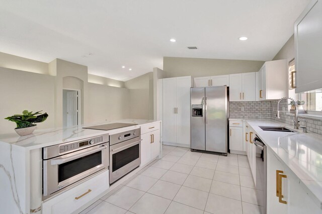 kitchen with lofted ceiling, sink, light stone countertops, white cabinets, and appliances with stainless steel finishes