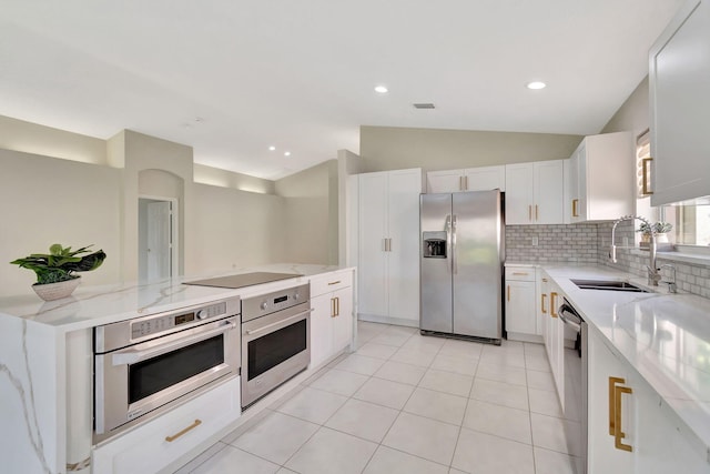 kitchen with a sink, stainless steel appliances, decorative backsplash, light stone countertops, and vaulted ceiling