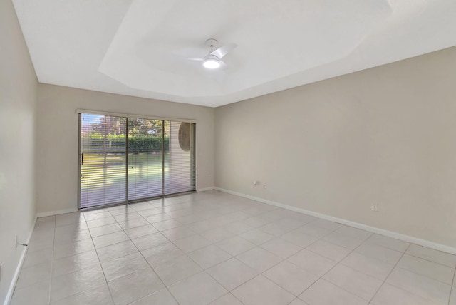 tiled empty room featuring a raised ceiling and ceiling fan