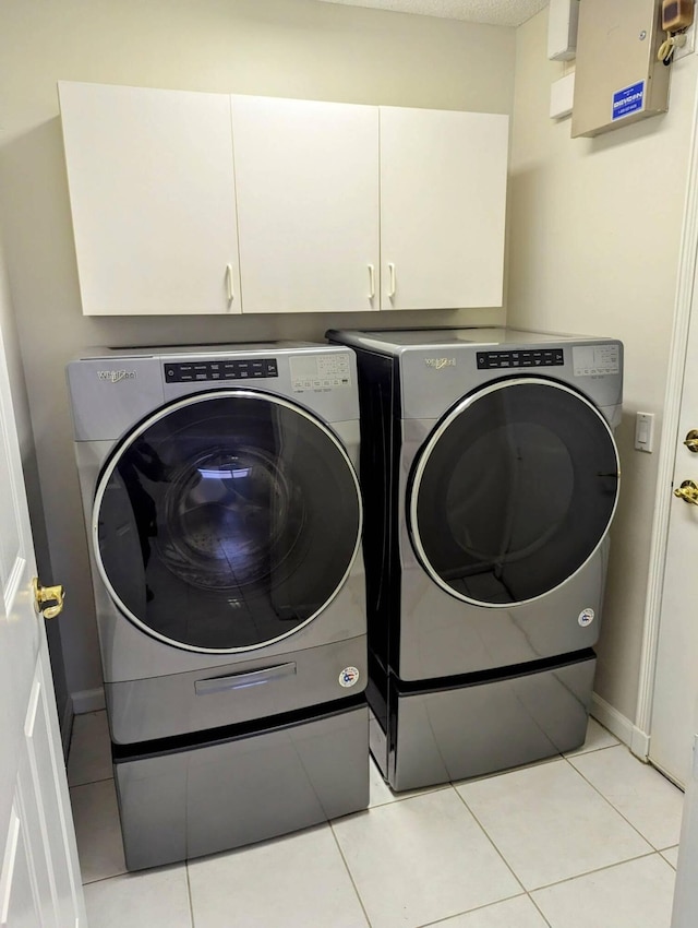 laundry room with cabinet space, light tile patterned floors, washing machine and dryer, and baseboards