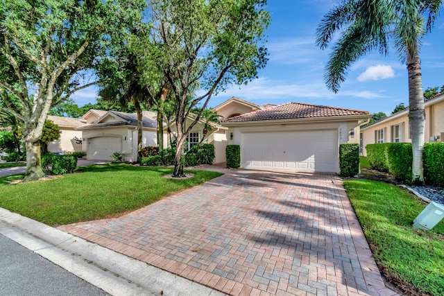 view of front of house featuring a tiled roof, a front yard, stucco siding, decorative driveway, and a garage