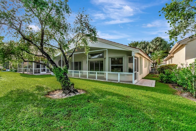 rear view of property featuring stucco siding, glass enclosure, and a yard