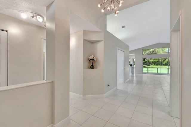 hall with vaulted ceiling, a textured ceiling, an inviting chandelier, and light tile patterned floors