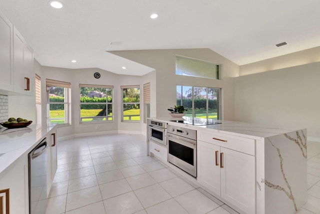 kitchen featuring vaulted ceiling, white cabinets, light stone counters, and stainless steel appliances