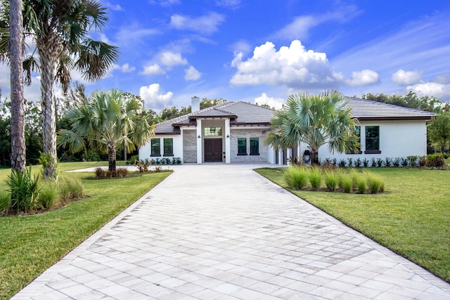 view of front of house featuring stucco siding, a front lawn, a tile roof, decorative driveway, and a chimney