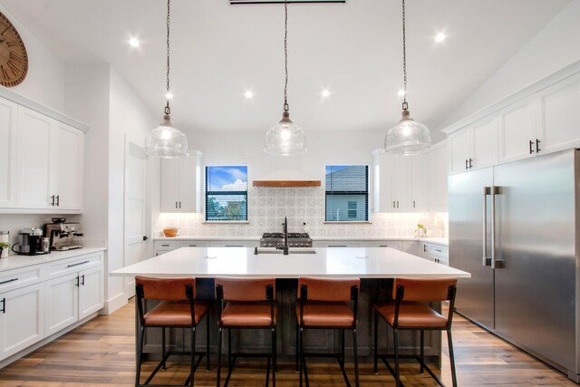 kitchen featuring decorative light fixtures, appliances with stainless steel finishes, white cabinetry, and a kitchen island with sink