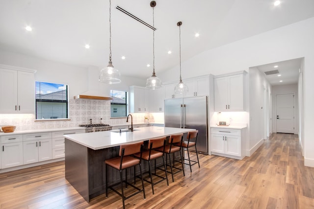 kitchen featuring stainless steel appliances, an island with sink, sink, vaulted ceiling, and light hardwood / wood-style floors