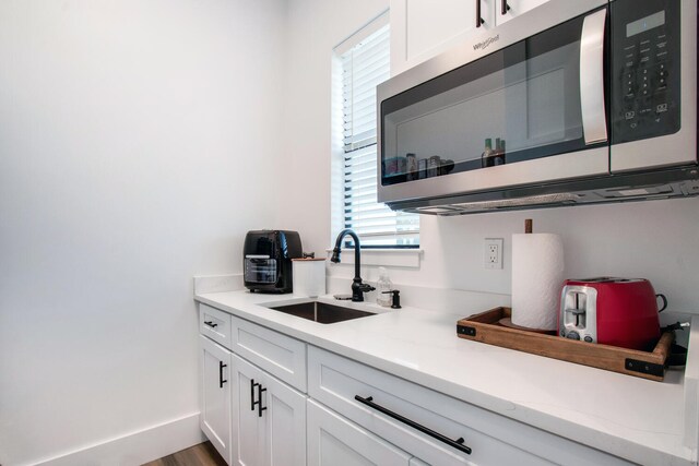 bar featuring white cabinets, wood-type flooring, light stone counters, and sink