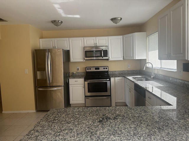 kitchen with dark stone counters, light tile patterned floors, white cabinets, stainless steel appliances, and a sink